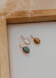 Three gold pendant necklaces with gemstones on a white surface with a wooden frame.