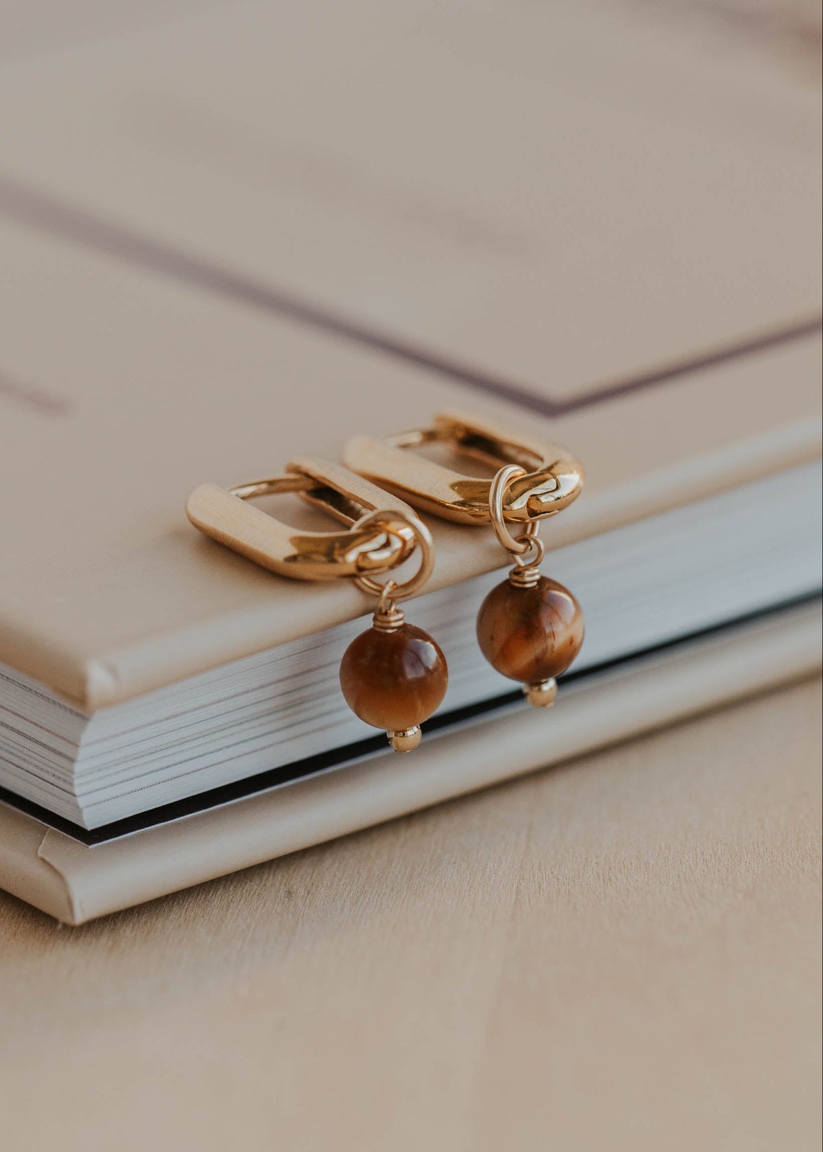 Gold earrings with brown beads on a beige surface