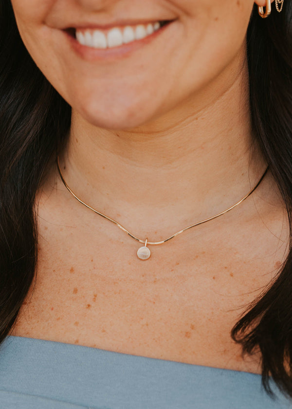 Close-up of a person wearing a delicate gold necklace with a small pendant.