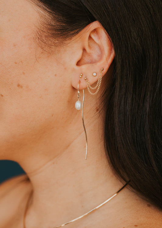 Close-up of a person wearing gold earrings and a necklace with a blurred background
