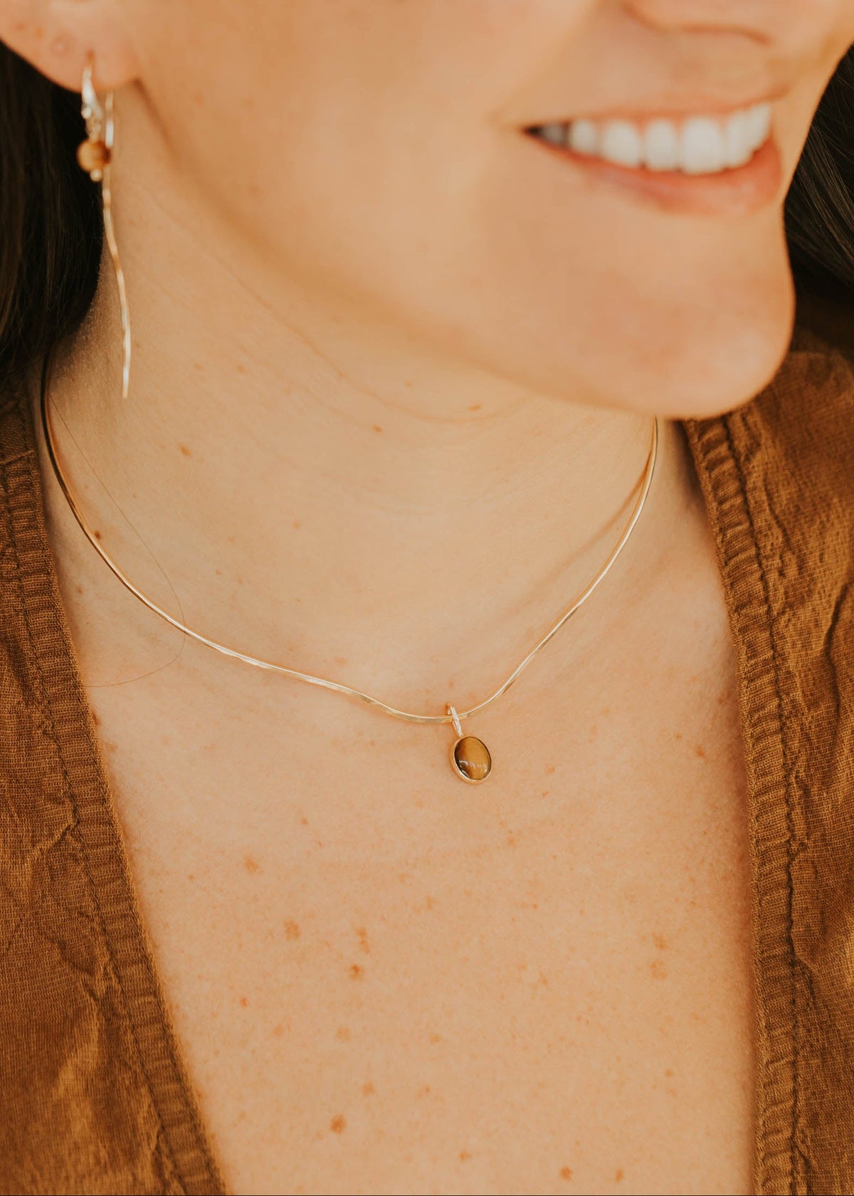 Woman wearing a gold necklace with a small pendant, smiling.