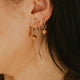 Close-up of an ear with gold earrings against a dark background