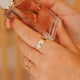 Hand holding a small transparent perfume bottle with a gold cap against a blurred background
