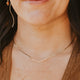 Woman with dark hair and a gold necklace, wearing a brown top.
