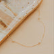 Gold necklace on a textured beige surface with a dish in the background