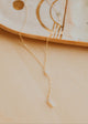 Gold necklace on a beige surface with a decorative dish in the background
