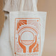 Tote bag with 'Hello Adorn' design held by a person wearing a beige sweater and pants.