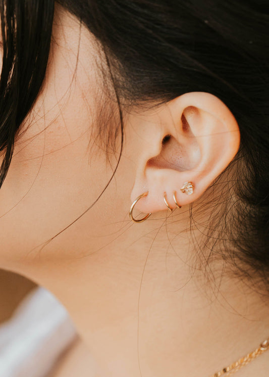 Close-up of a person wearing gold hoop earrings and a delicate necklace.