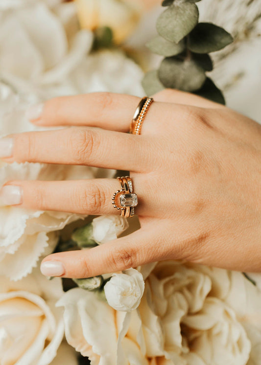 Hand wearing a ring with a bouquet of flowers in the background