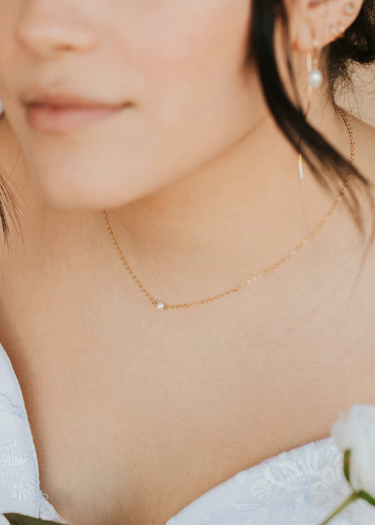 Close-up of a person wearing a delicate gold necklace and earrings, with a blurred background.
