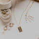 Gold jewelry including a necklace, earrings, and rings on a light surface with a white flower.