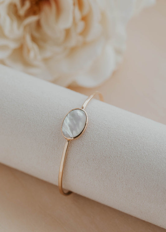Gold bracelet with a stone on a white cushion, with a blurred flower in the background