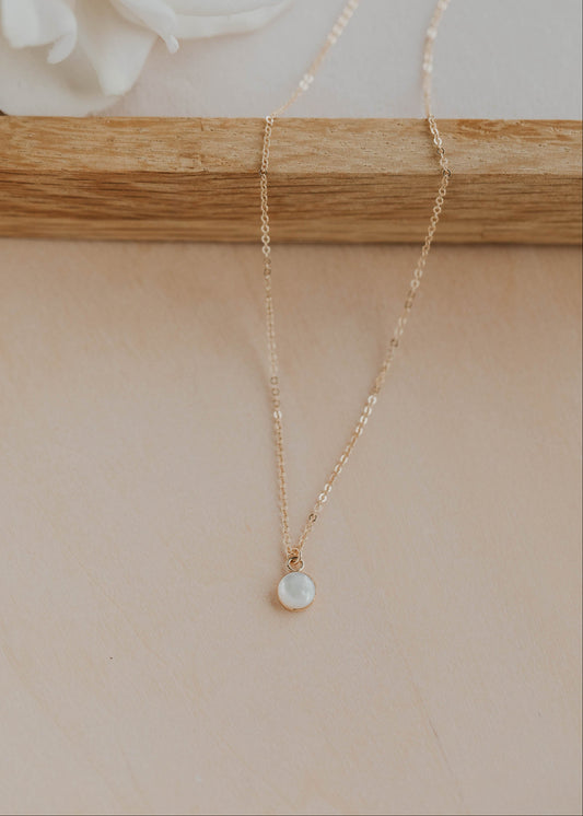 Gold necklace with a pearl pendant on a beige surface