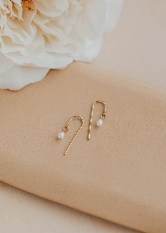 Gold earrings with pearls on a beige surface with a white flower.