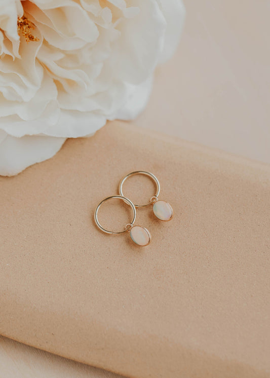 Gold earrings on a beige surface with a white flower in the background