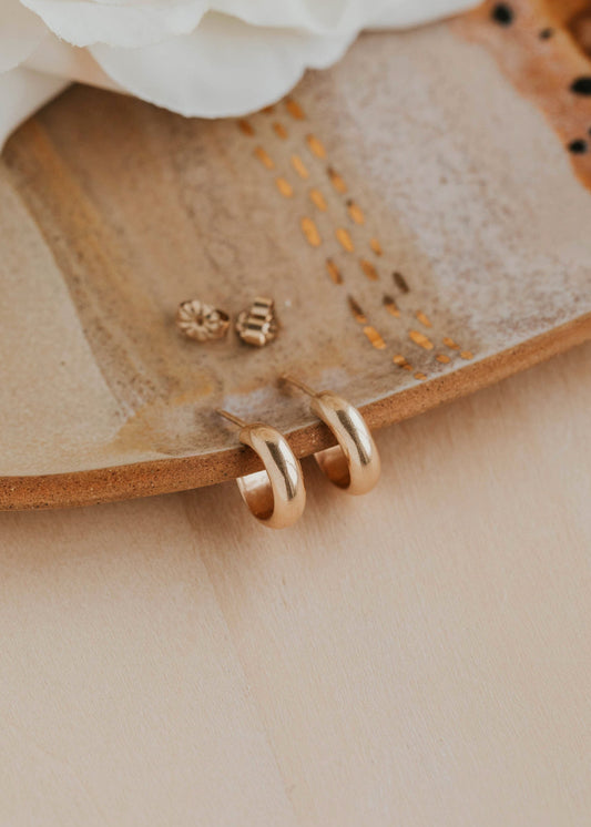 Gold earrings on a textured beige surface with white flowers in the background