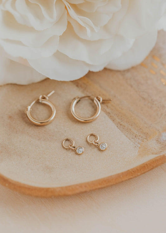Gold hoop earrings with small gemstones on a wooden surface with white flowers in the background