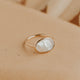 Gold ring with a white stone on a beige surface