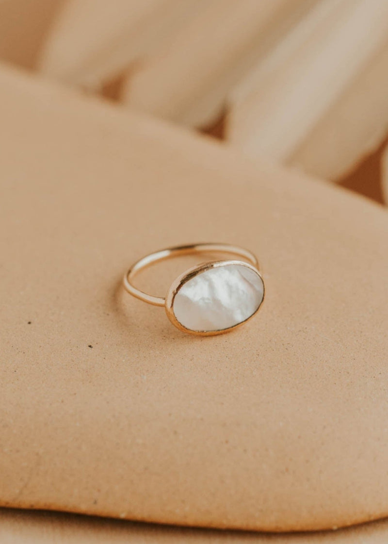 Gold ring with a white stone on a beige surface