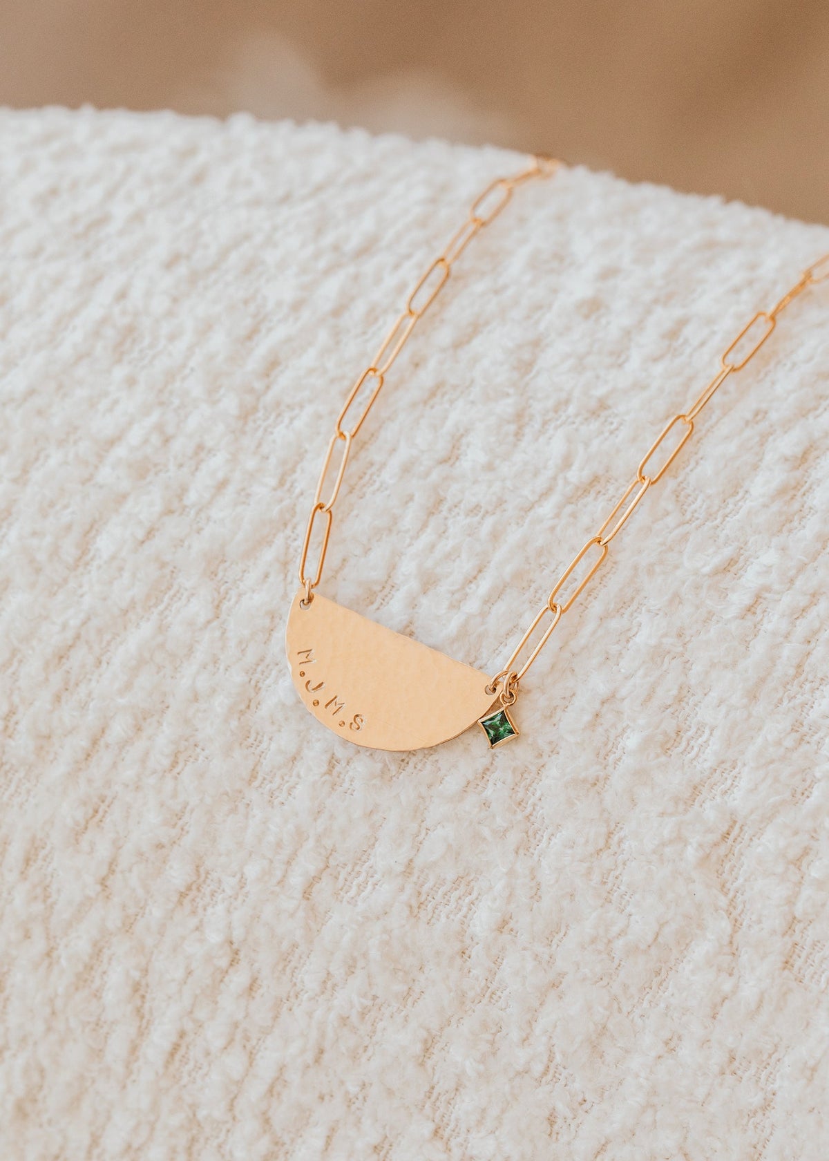 Gold necklace with a green gemstone on a textured beige surface