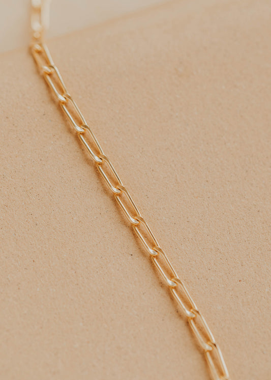Gold chain necklace on a person's neck against a beige background