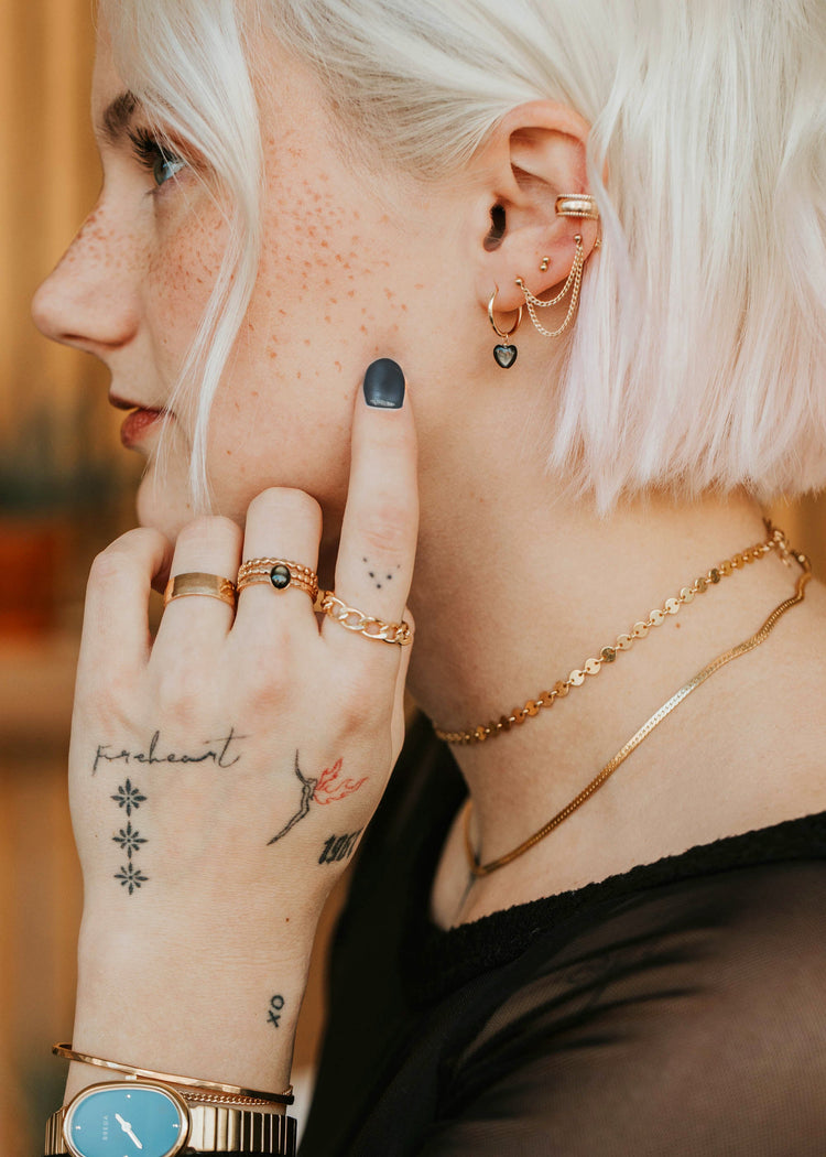 Person with tattoos on hand, wearing gold jewelry and a black top.