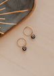 Gold hoop earrings with black heart charms on a wooden surface.