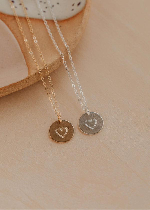 Two necklaces with heart pendants on a beige surface