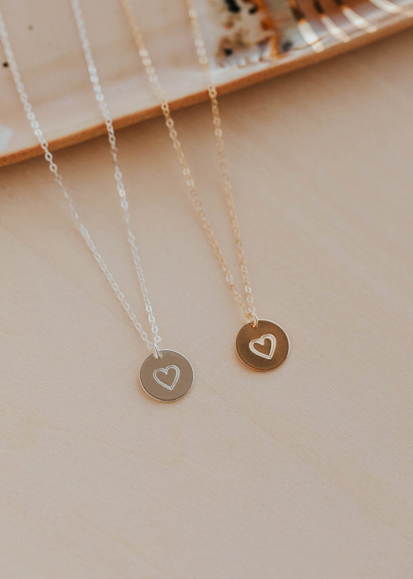 Two necklaces with heart pendants on a beige surface