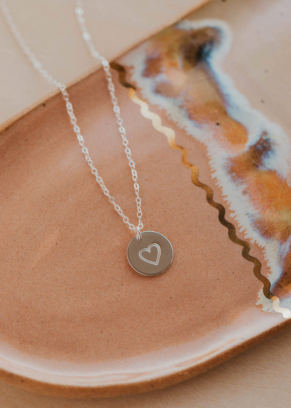 Silver necklace with a heart pendant on a ceramic plate