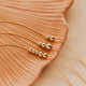 Gold Hello adorn beaded necklaces on a textured beige surface