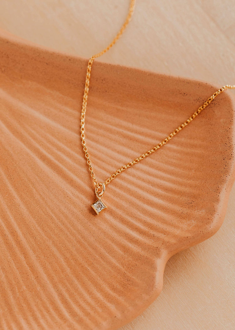 Gold necklace with a diamond pendant on a textured beige surface