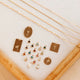 Collection of gold necklaces and pendants displayed on a white surface with a wooden frame.