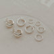 Set of silver hoop earrings on a light gray surface with 'indigo' branding.
