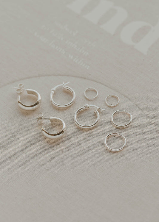 Set of silver hoop earrings on a light gray surface with 'indigo' branding.