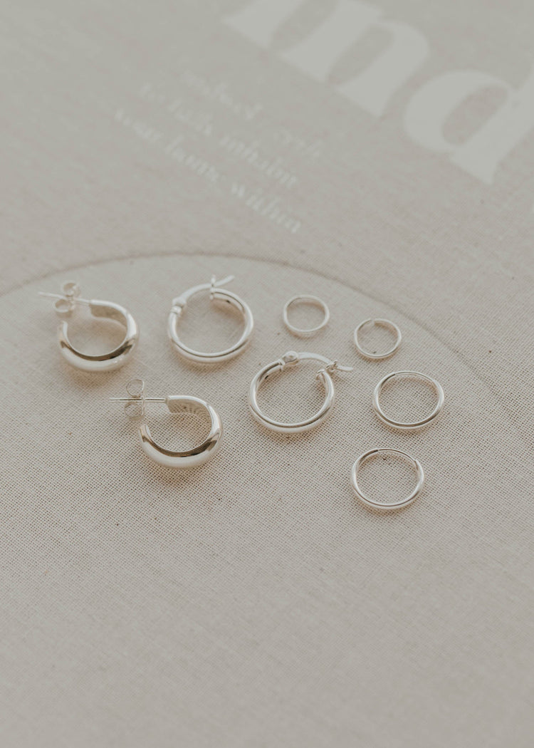 Set of silver hoop earrings on a light gray surface with 'indigo' branding.