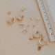 Collection of gold earrings on a beige surface with a ruler for scale.