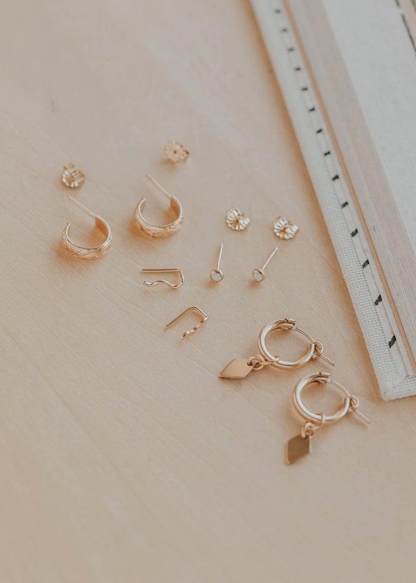 Collection of gold earrings on a beige surface with a ruler for scale.