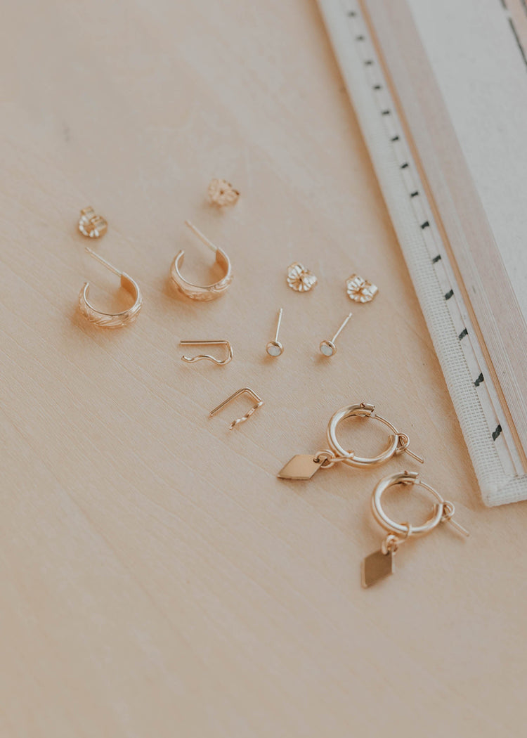 Collection of gold earrings on a beige surface with a ruler for scale.