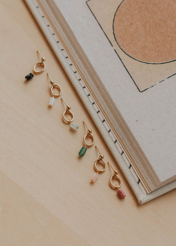 Gold earrings with colorful beads on a beige surface