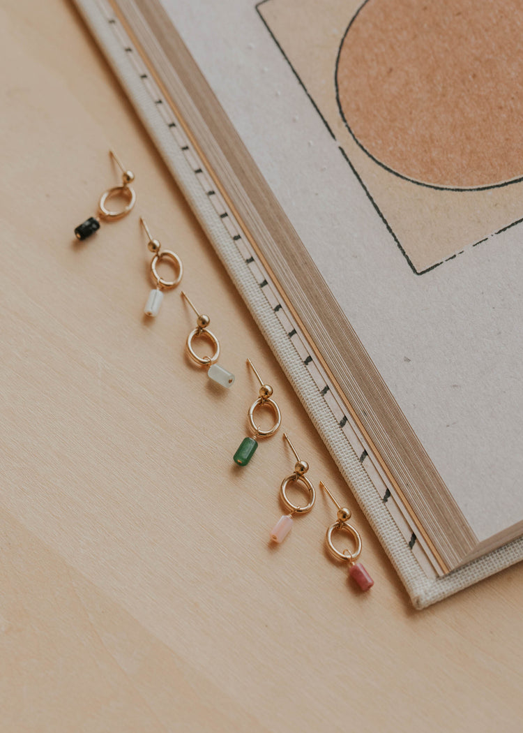 Gold earrings with colorful beads on a beige surface