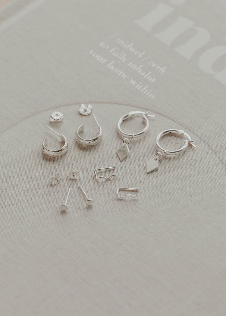 Set of silver earrings on a clear stand with a light gray background