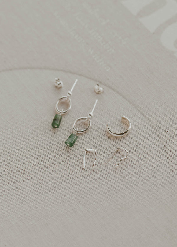 Collection of small silver and green earrings on a light gray background