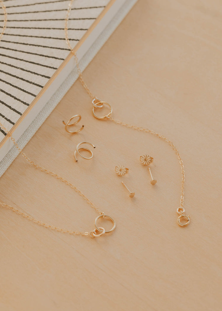 Gold jewelry set including necklaces and earrings on a beige surface with a striped fabric background.