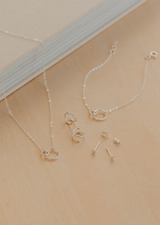 Silver jewelry set including necklaces and earrings on a beige surface.