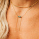 Close-up of a person wearing a gold necklace with a green gemstone on a white background