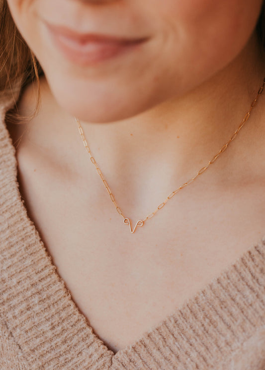 Close-up of a person wearing a delicate gold necklace with a uterus design.