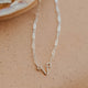 A gold-colored necklace with a simple, uterus pendant laid out on a light surface.