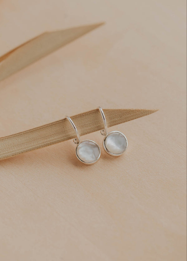 Pair of silver earrings with round gemstones on a beige background