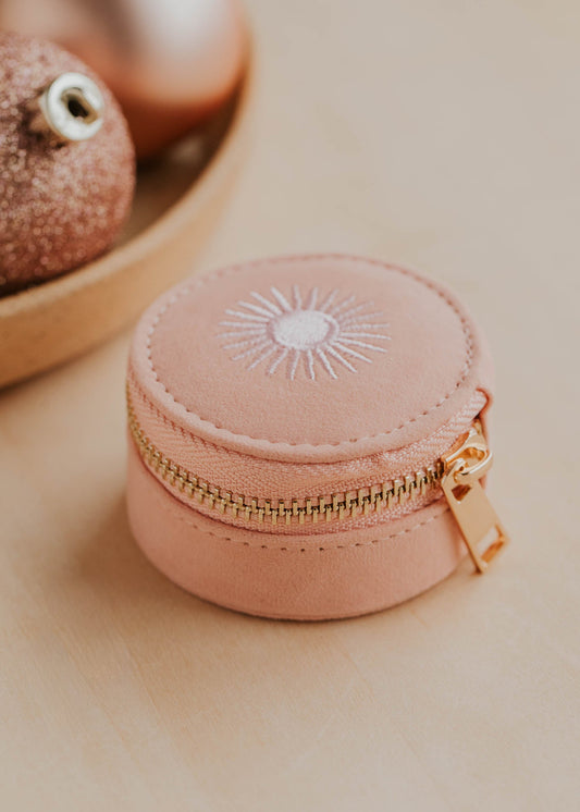 Pink jewelry box with gold zipper on a beige surface with decorative spheres in the background